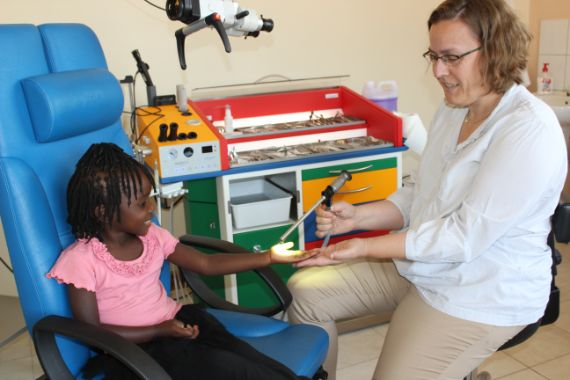 Ein kleines Mädchen sitzt auf einem Behandlungsstuhl und wird von einer Ärztin untersucht.