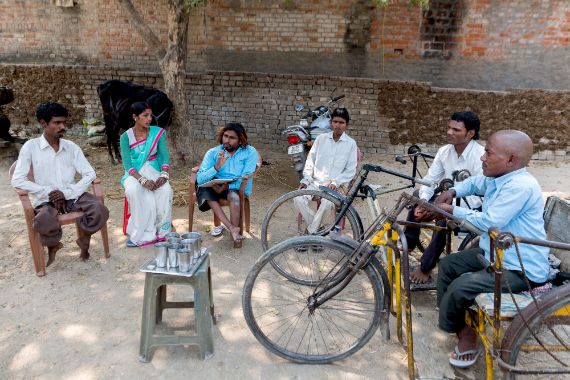 Männer und Frauen, zwei mit Tricyle, sitzen im Kreis.