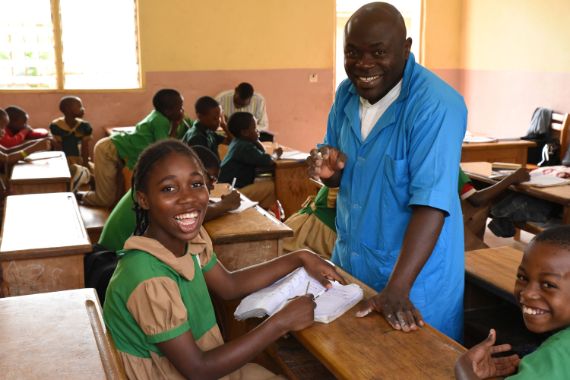 Ein lachendes Mädchen und ein Mann in einem Klassenzimmer mit weiteren Kindern
