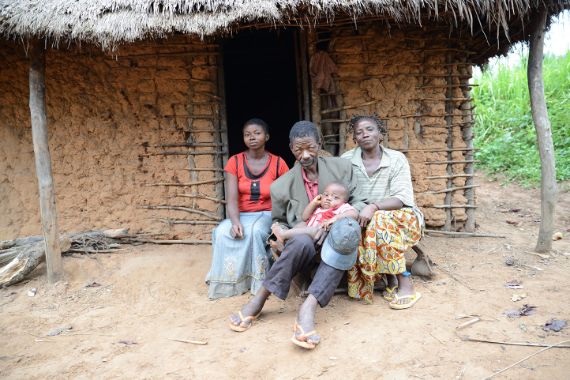 Zwei Frauen und ein Mann sitzen vor einer Hütte.