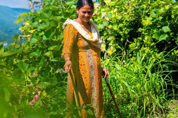 Frau mit Gehstock bewässert ihren Garten.