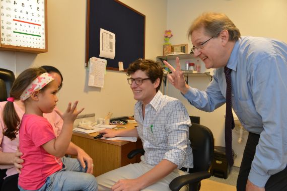 Augenarzt Dr. Duerksen und ein Mitarbeiter führen einen Sehtest mit einem kleinen Mädchen durch.