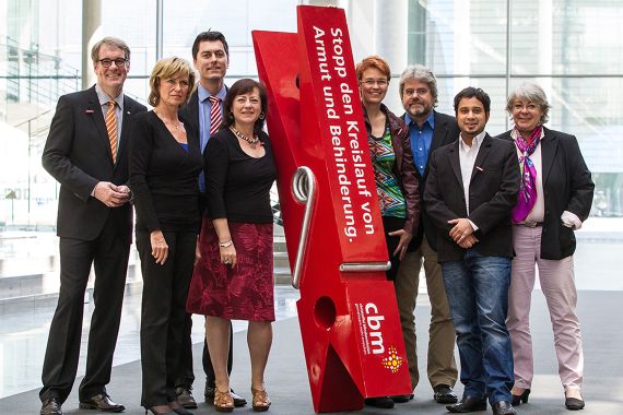 Auf dem Foto steht eine Gruppe von acht Personen neben eine überdimensionalen Wäscheklammer. Auf der Klammer steht: Stoppt den Kreislauf von Armut und Behinderung.