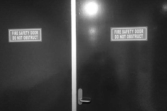 Zwei schwarze Türen, darauf Schilder mit dem Text: Fire Safety Door Do Not Obstruct.