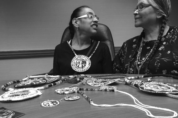 Zwei Frauen sitzen an einem Tisch voller Ketten, wie sie selbst welche als Schmuckstück tragen.