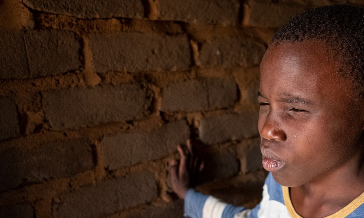 Ein Junge mit zusammengekniffenen Augen hat eine Hand auf eine Backsteinwand gelegt.