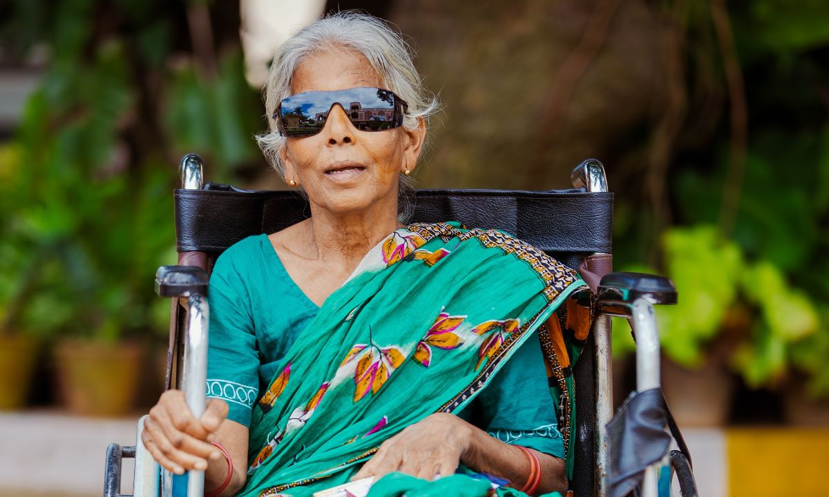 Eine Frau im Sari sitzt im Rollstuhl. Sie trägt eine auffällige Sonnenbrille mit verspiegelten Gläsern.