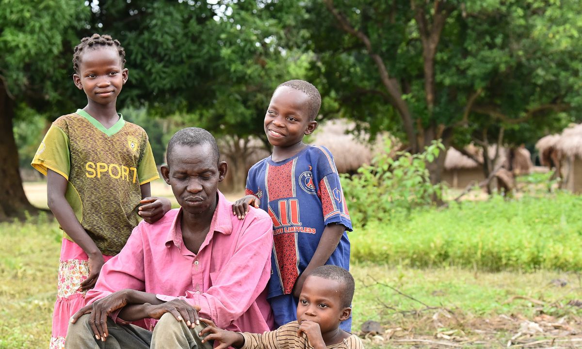 Drei Kinder stehen hinter einem sitzenden Mann Mitte vierzig.