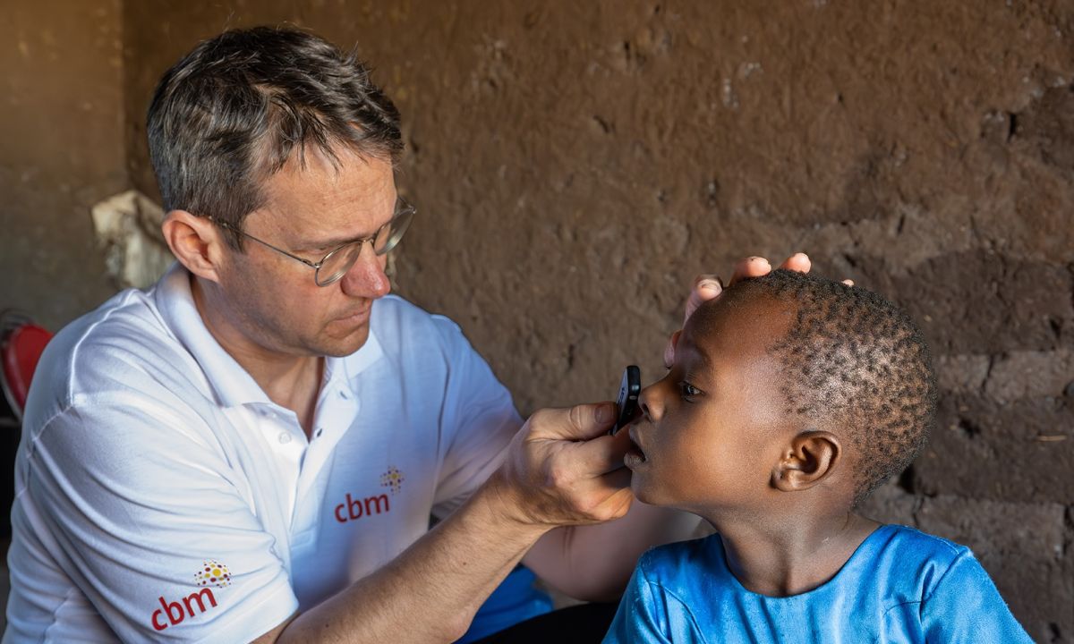 Ein Mann im weißen Polohemd mit CBM-Logo untersucht die Augen eines kleinen Mädchens.