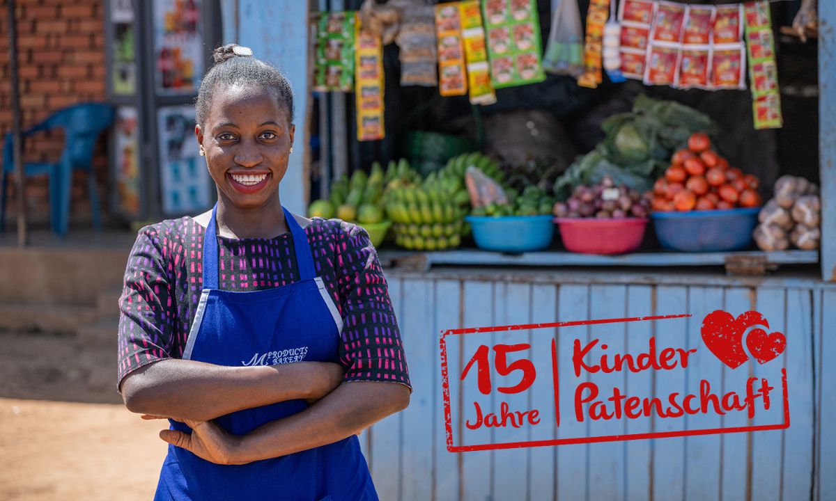 Eine junge, lachende Frau mit Schürze steht vor einem Stand mit Obst und Gemüse. Stempel auf dem Bild: 15 Jahre Kinderpatenschaft