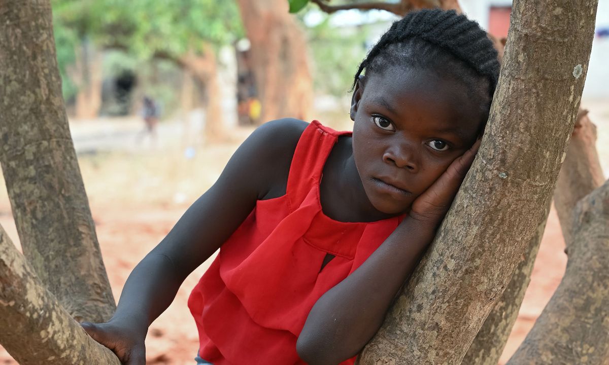 Ein kleines Mädchen schmiegt sich an den Ast eines Baums.
