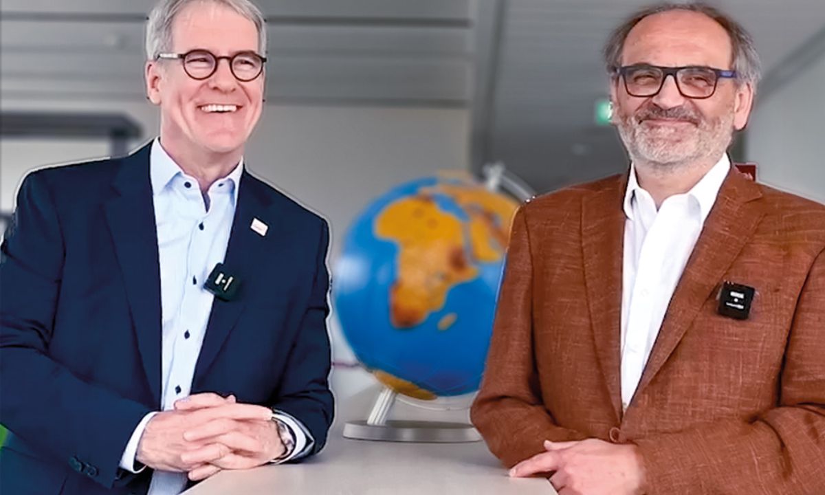 Zwei lachende Herren im Anzug vor einem Globus.