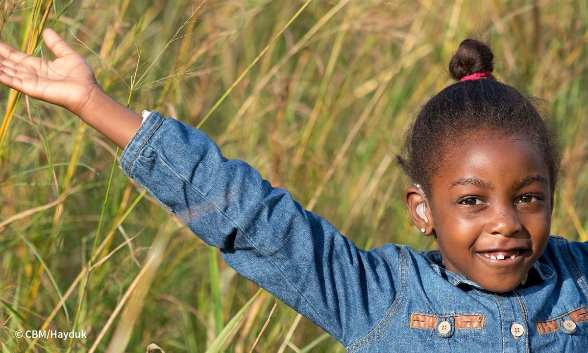 Mädchen mit Hörgerät und ausgebreiteten Armen