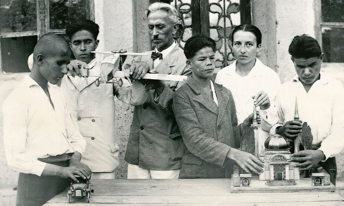 Ein Mann, eine Frau und einige Jugendliche betasten ein Flugzeugmodell und das Modell  eines Gebäudes