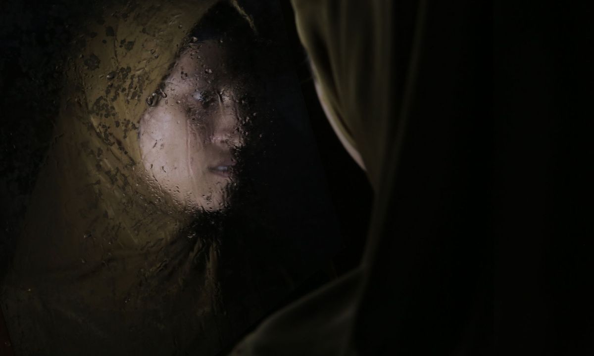 Eine Frau mit gelbem Kopftuch vor einem nassen Spiegel. Ihr Gesicht ist im Spiegel zu sehen.