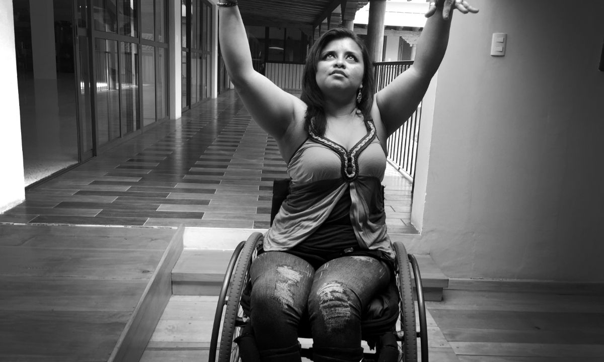 Eine Frau im Rollstuhl hebt elegant ihre Arme zu einer tanzenden Bewegung und folgt ihren Händen dabei mit ihrem Blick.