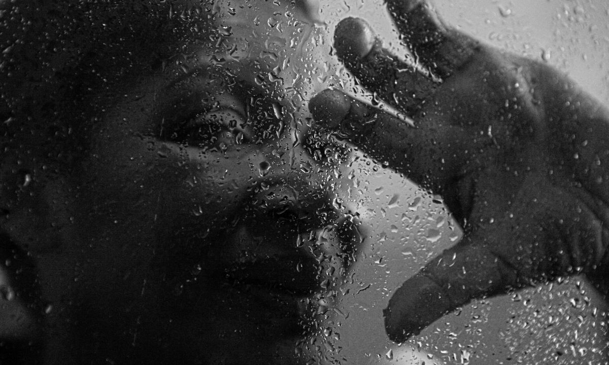 Gesicht einer Frau aus Lateinamerika hinter einer Glasscheibe, an die sie mit der Hand fasst